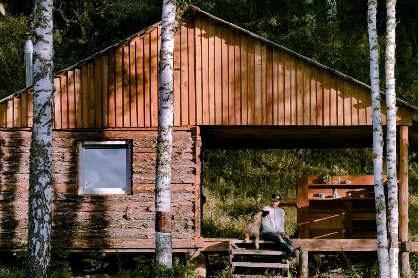 Owner and dog on the porch of a forest cabin