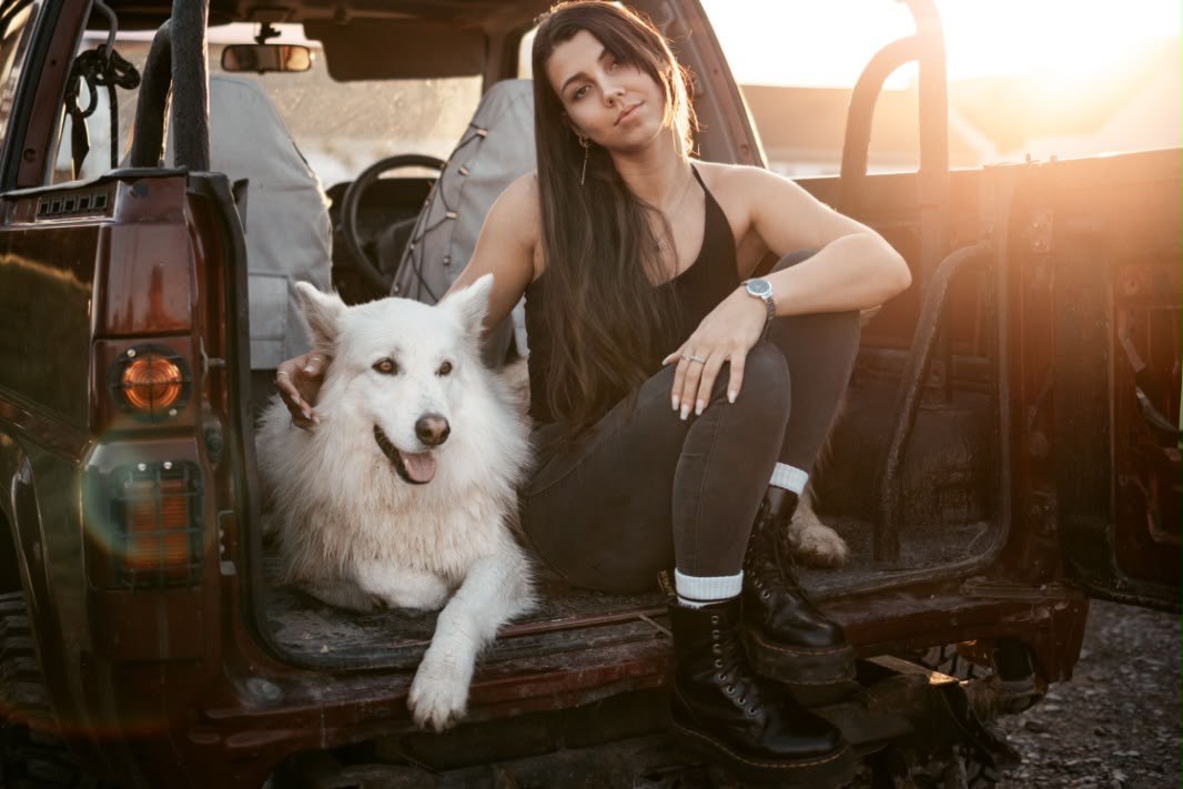 Woman and her white dog relaxing in the back of a 4x4 at sunset